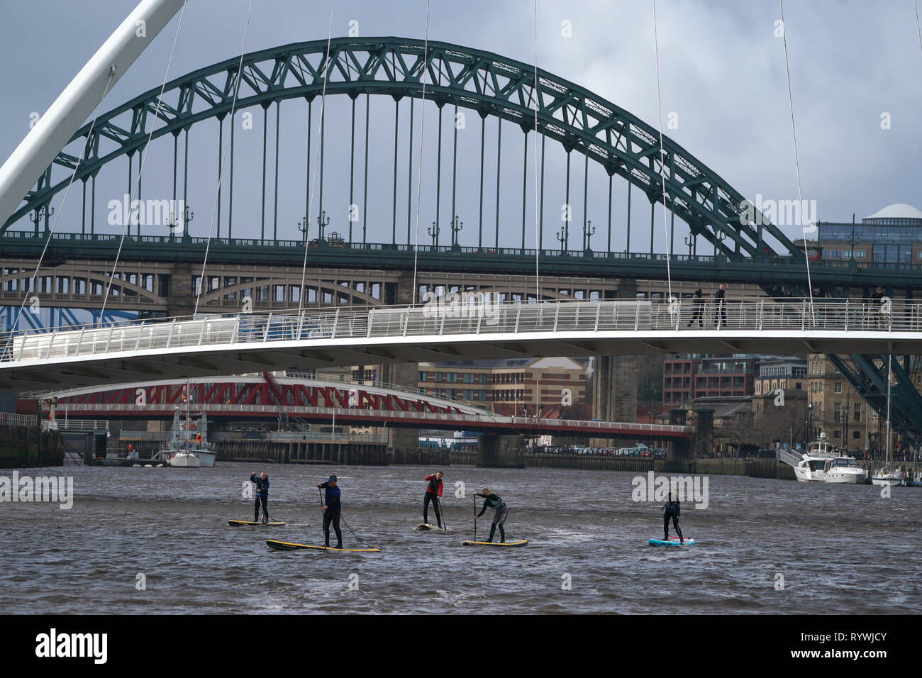Paddle boarders pass under the Gateshead Millennium Bridge spanning the River Tyne in Newcastle upon Tyne. Stock Photo