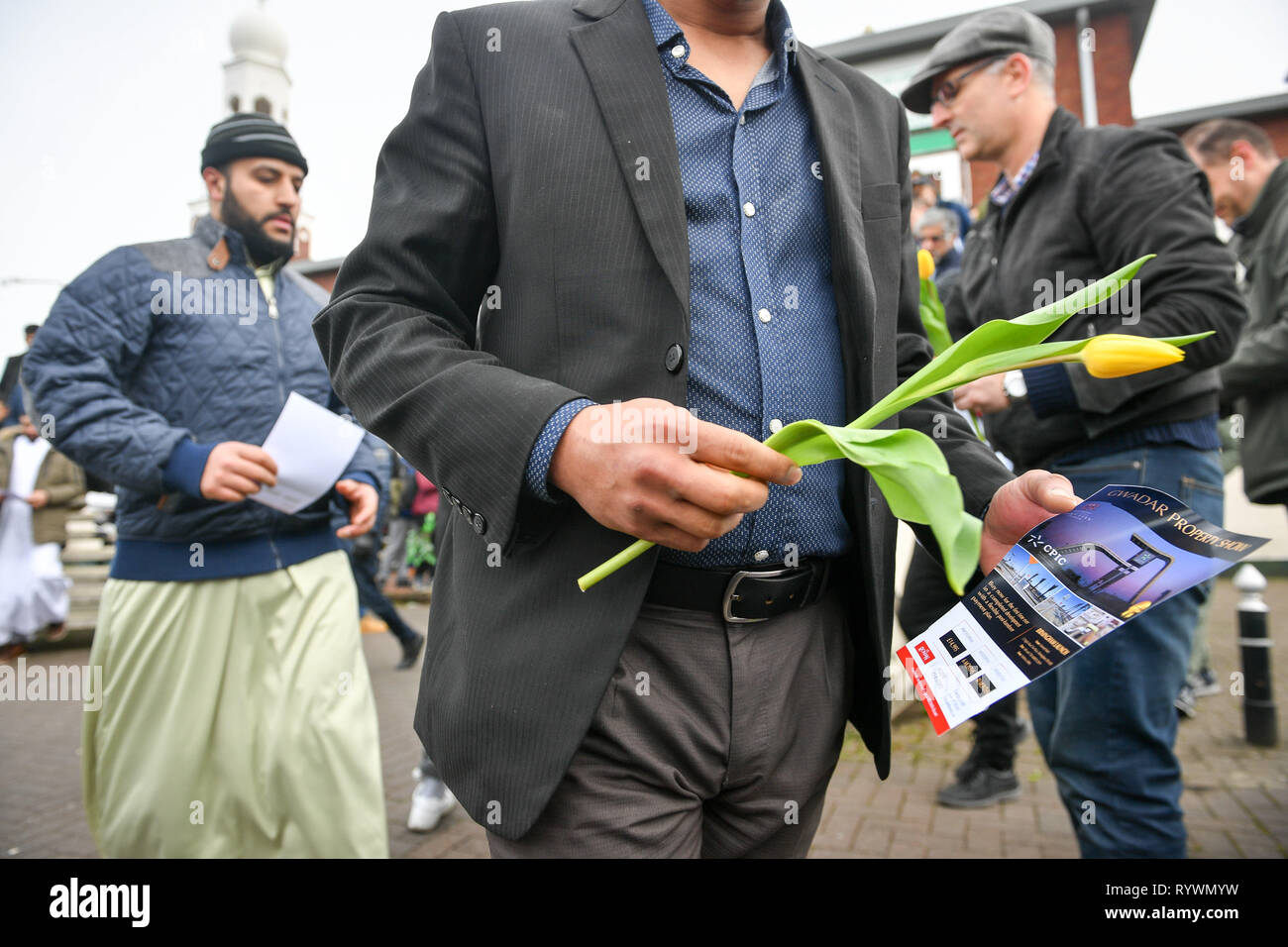 A Muslim man carries a yellow flower given to him by Christian James Lynch, from Riverside Church, outside Birmingham Central Mosque as Friday prayers finish after the attack on the Mosque in Christchurch, New Zealand. Stock Photo