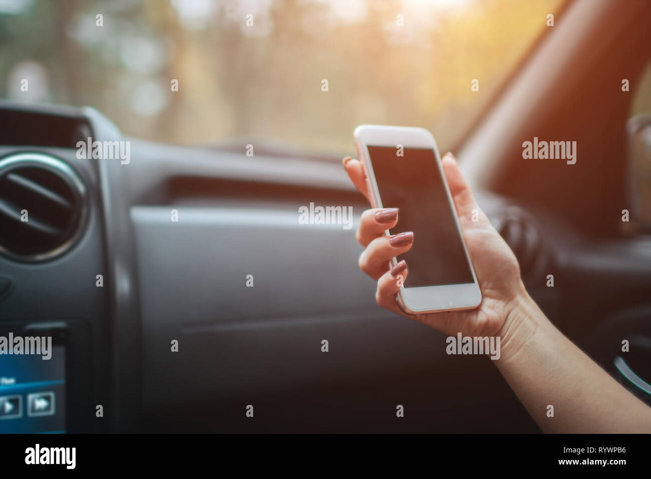 eautiful woman smiling while sitting on the front passenger seats in the car. Girl is using a smartphone. Hand closeup. Stock Photo