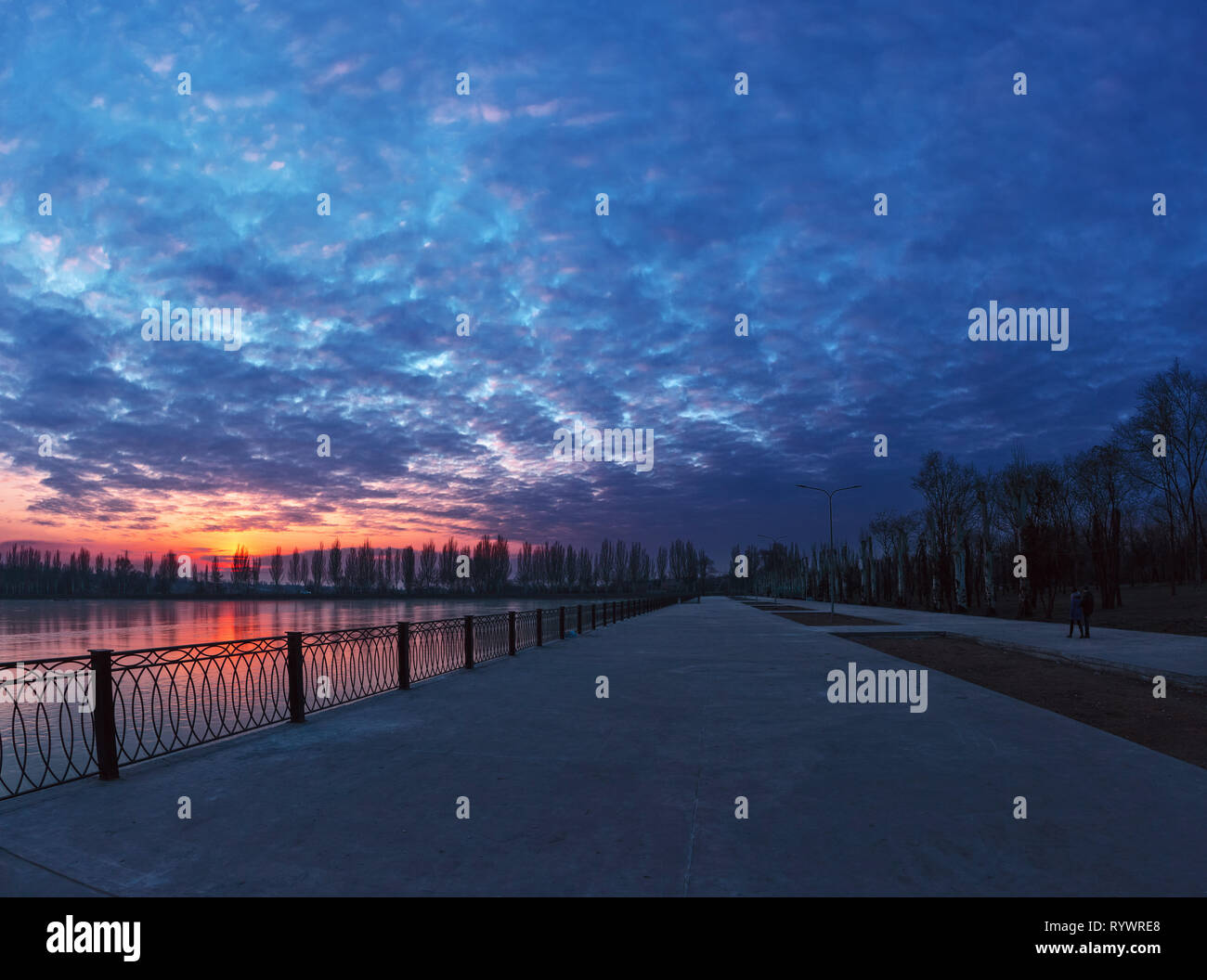 Fantastic bright cloudy sunset over the lake and the road. Winter landscape in the city Stock Photo