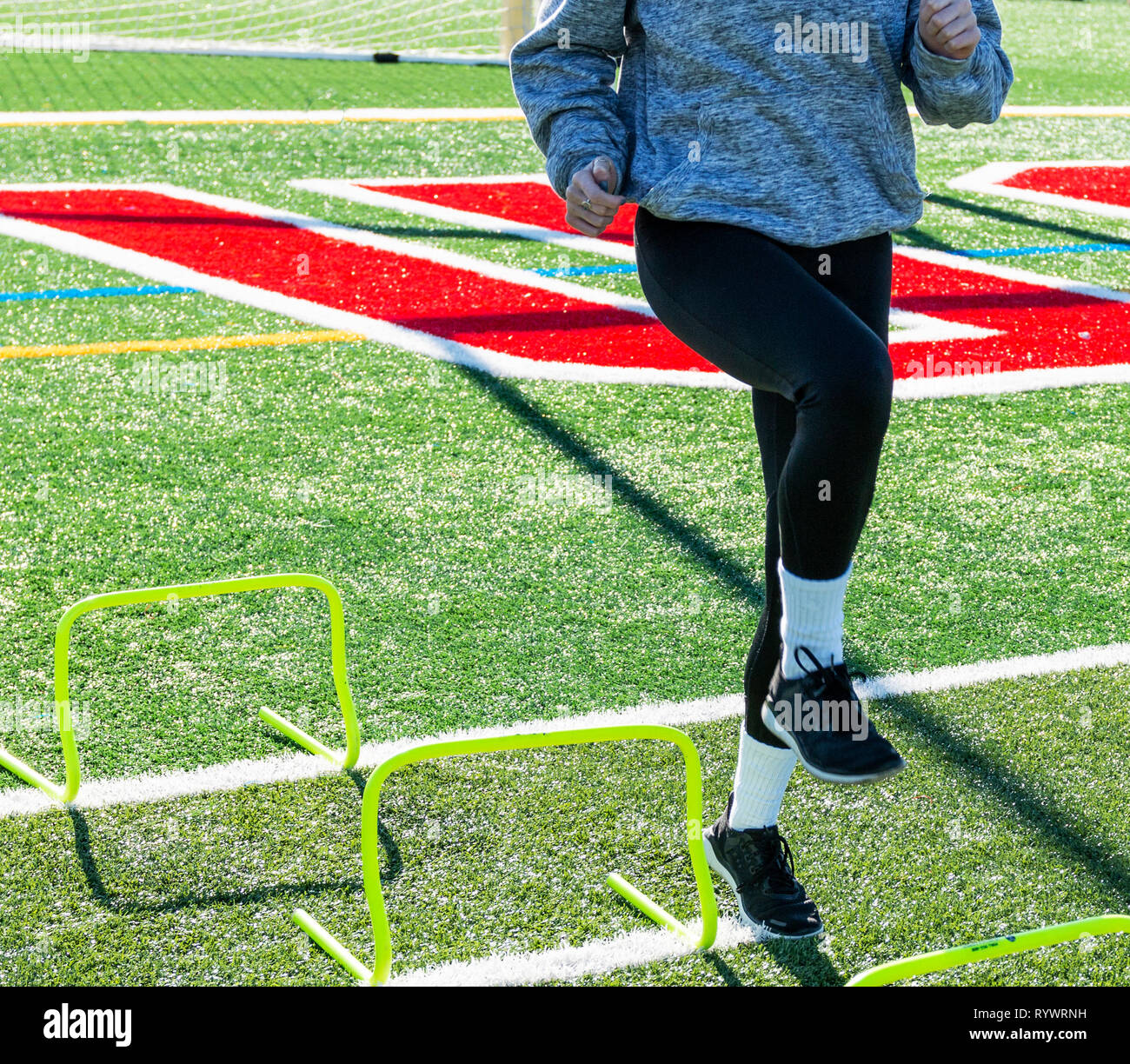 A high school girl is stepping over two foot yellow mini hurdles for