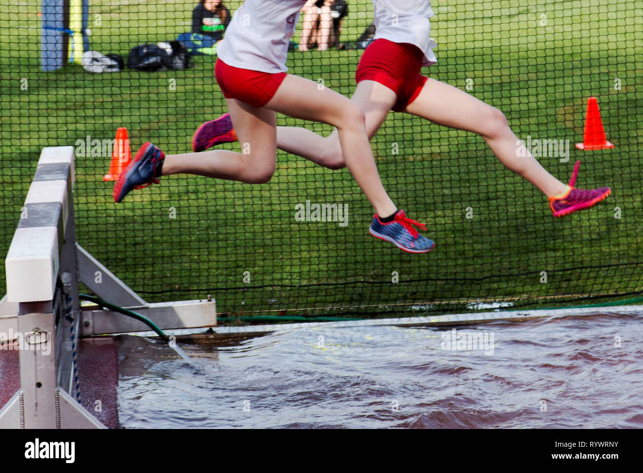 Two high school girls going over the water pit in a steeplechase race Stock Photo