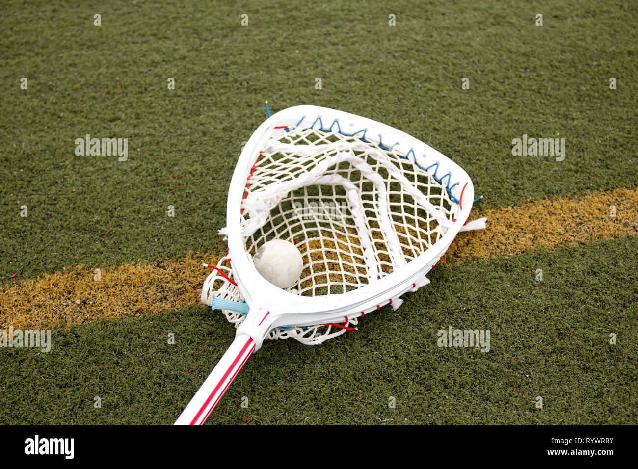 Lacrosse goalie stick with a ball in the netting on a green turf field