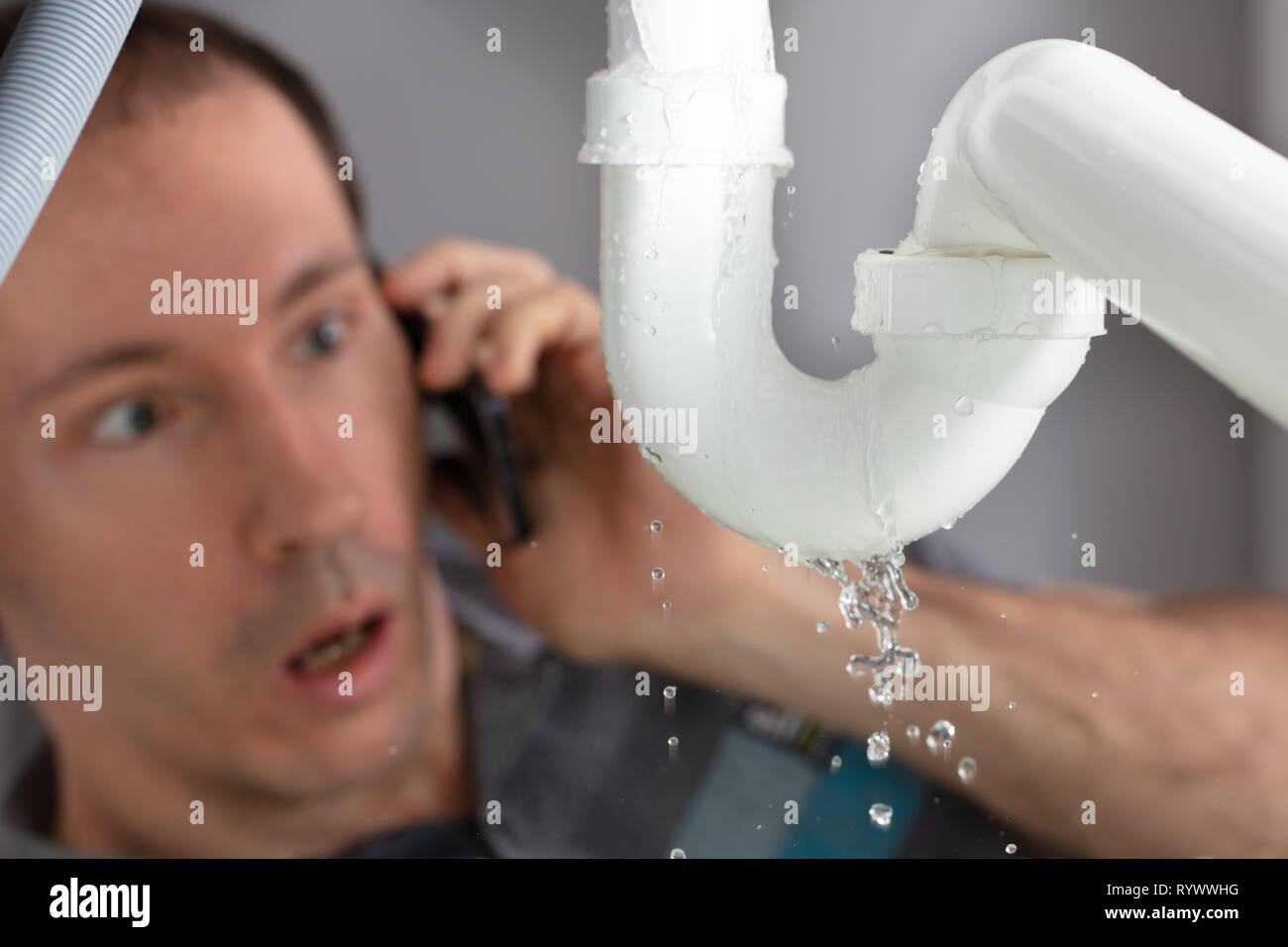 Shocked Young Man Calling Plumber To Fix Sink Pipe Leakage In Kitchen