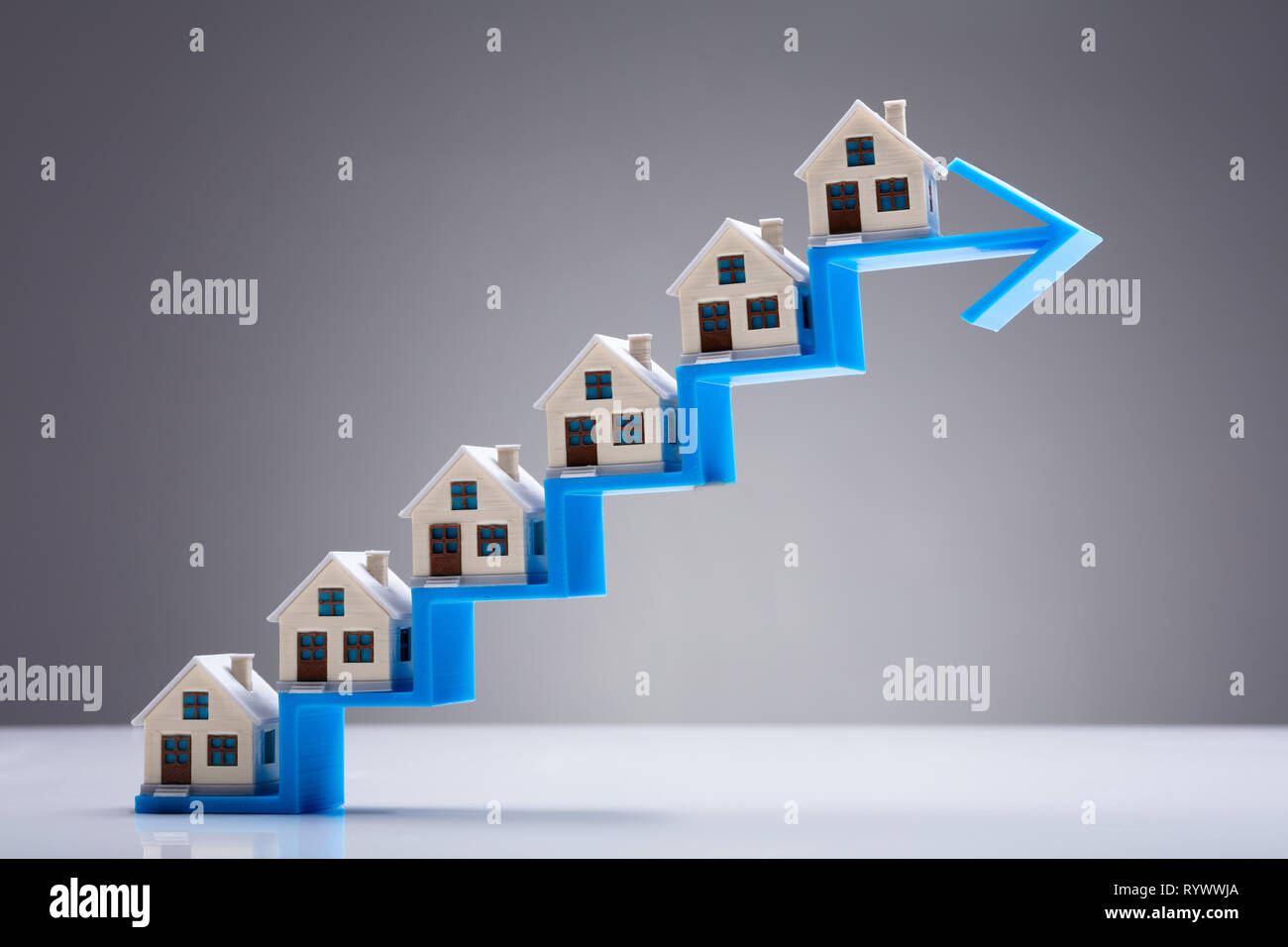 Small Model House On The Increasing Staircase Blue Arrow Over White Desk Stock Photo