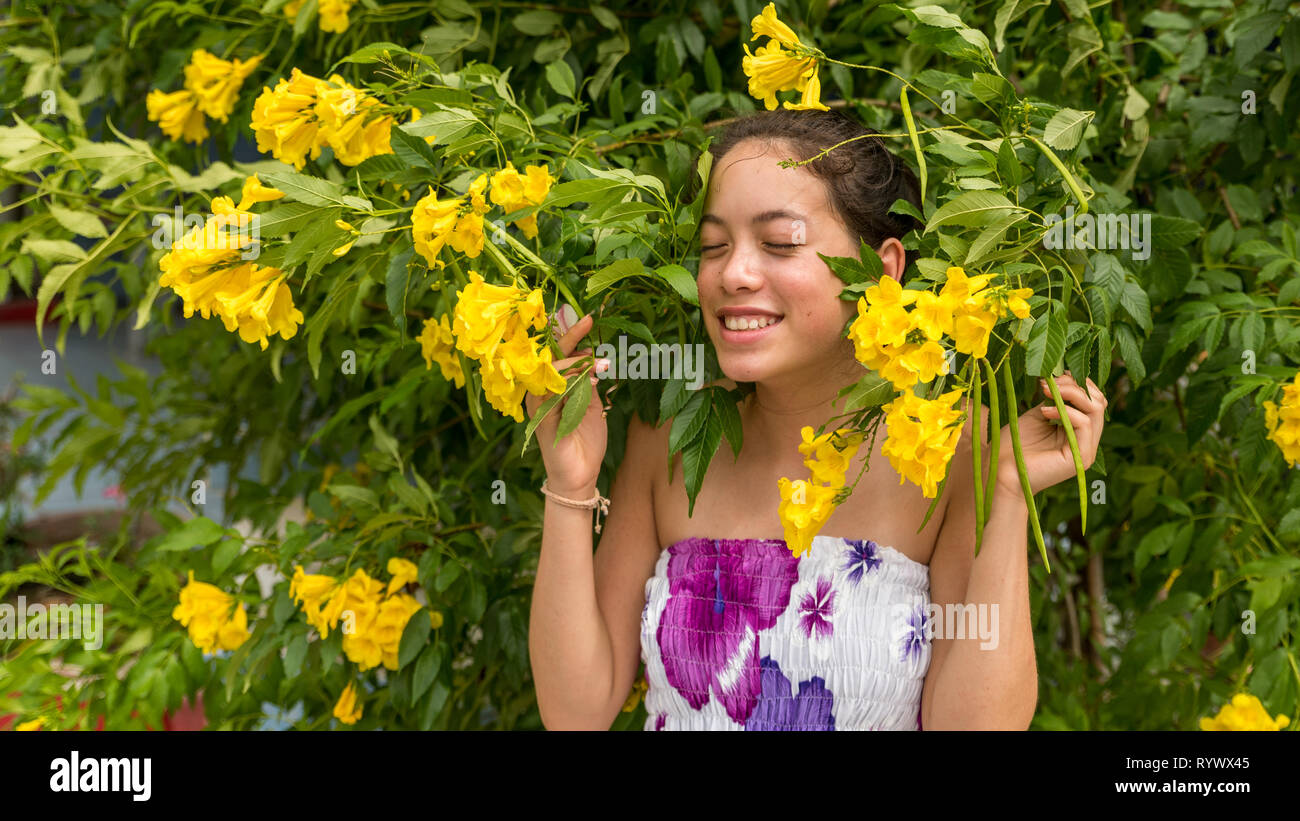 Young girl in flowered dress standing in front of flowers and smiling Stock Photo