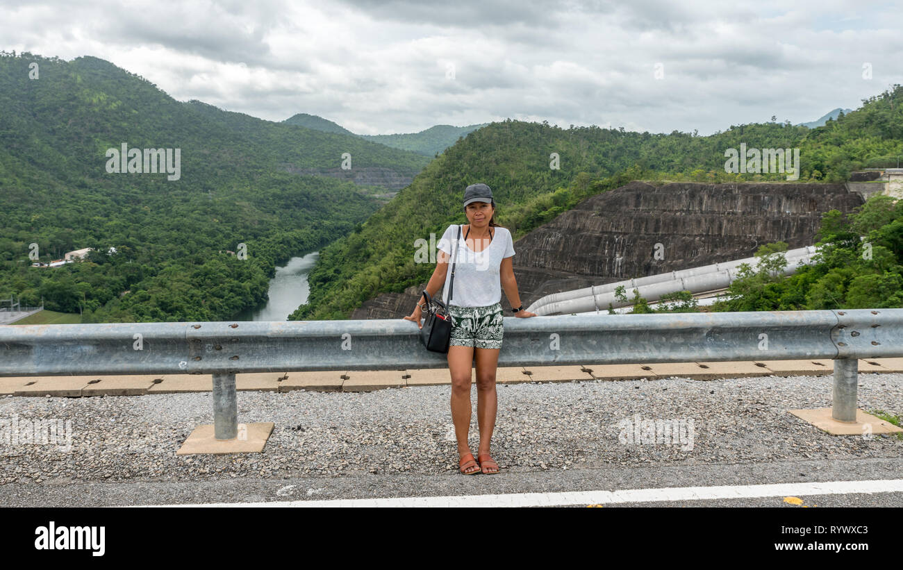Asian woman sitting on guard rail in Thailand with river in the background Stock Photo