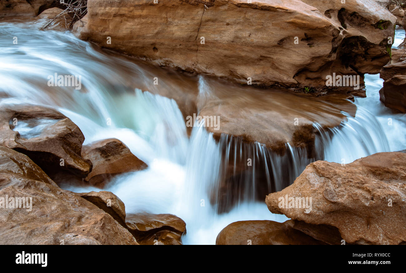 Water flowing and cascading through a sand stone slot canyon. Silky water effect with flowing blue water. Stock Photo