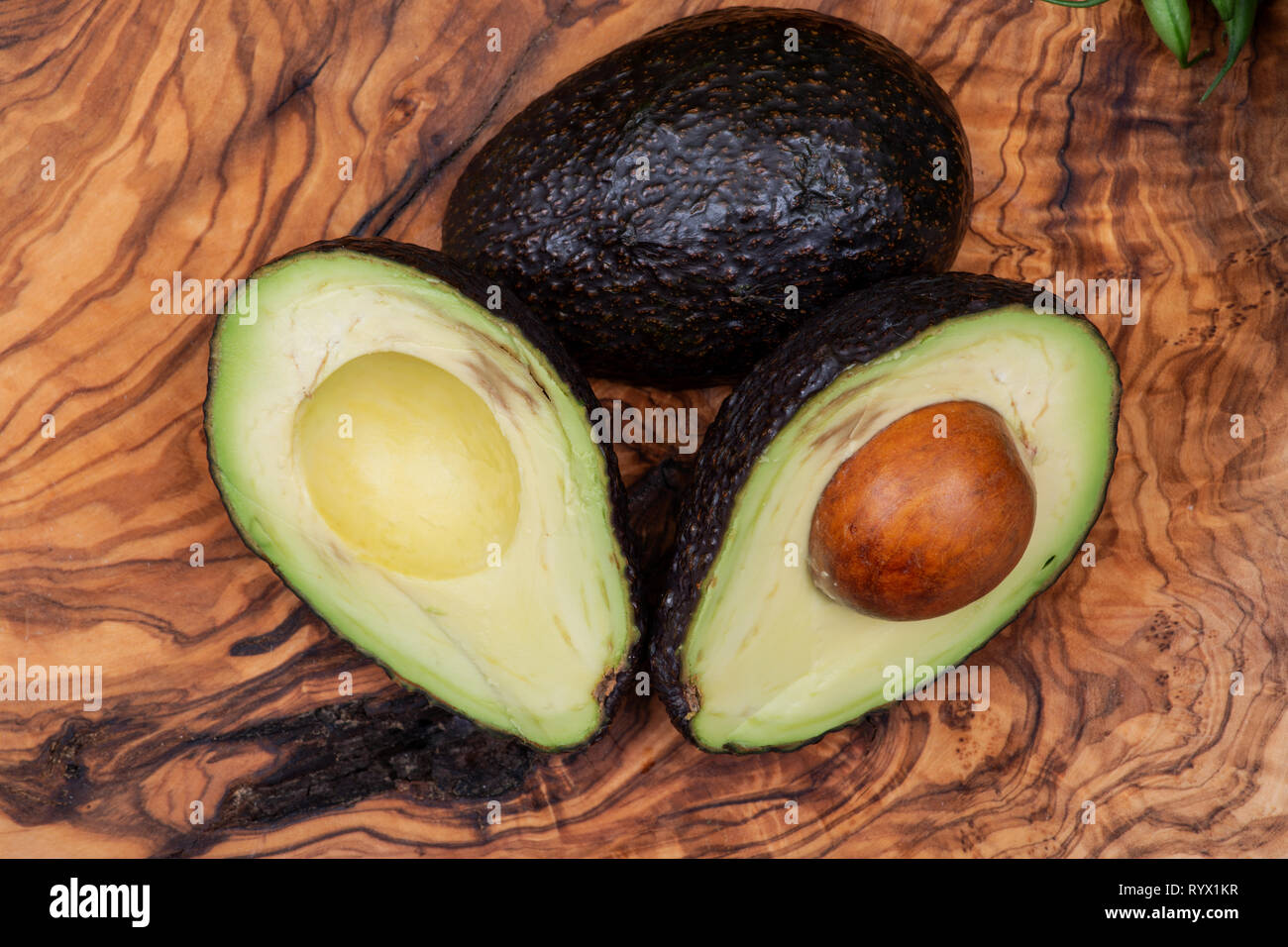 Fresh Organic Avocado cut in half arranged on natural olive wood. Persea americana in the Lauraceae family. Avocado Pear. Alligator Pear. Stock Photo