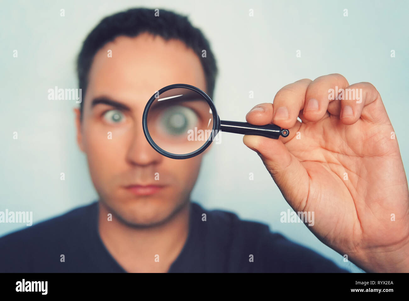 Male hand holding magnifying glass with blurred man's eye on foreground