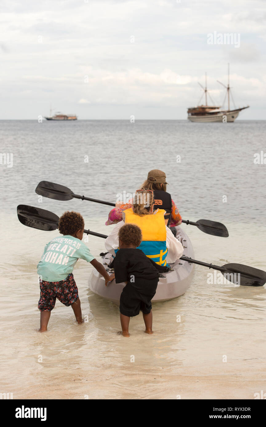 Pandora George and Claire Norrish launch their kayak with the help of local children on Sawandarek on island of Mansuar Stock Photo