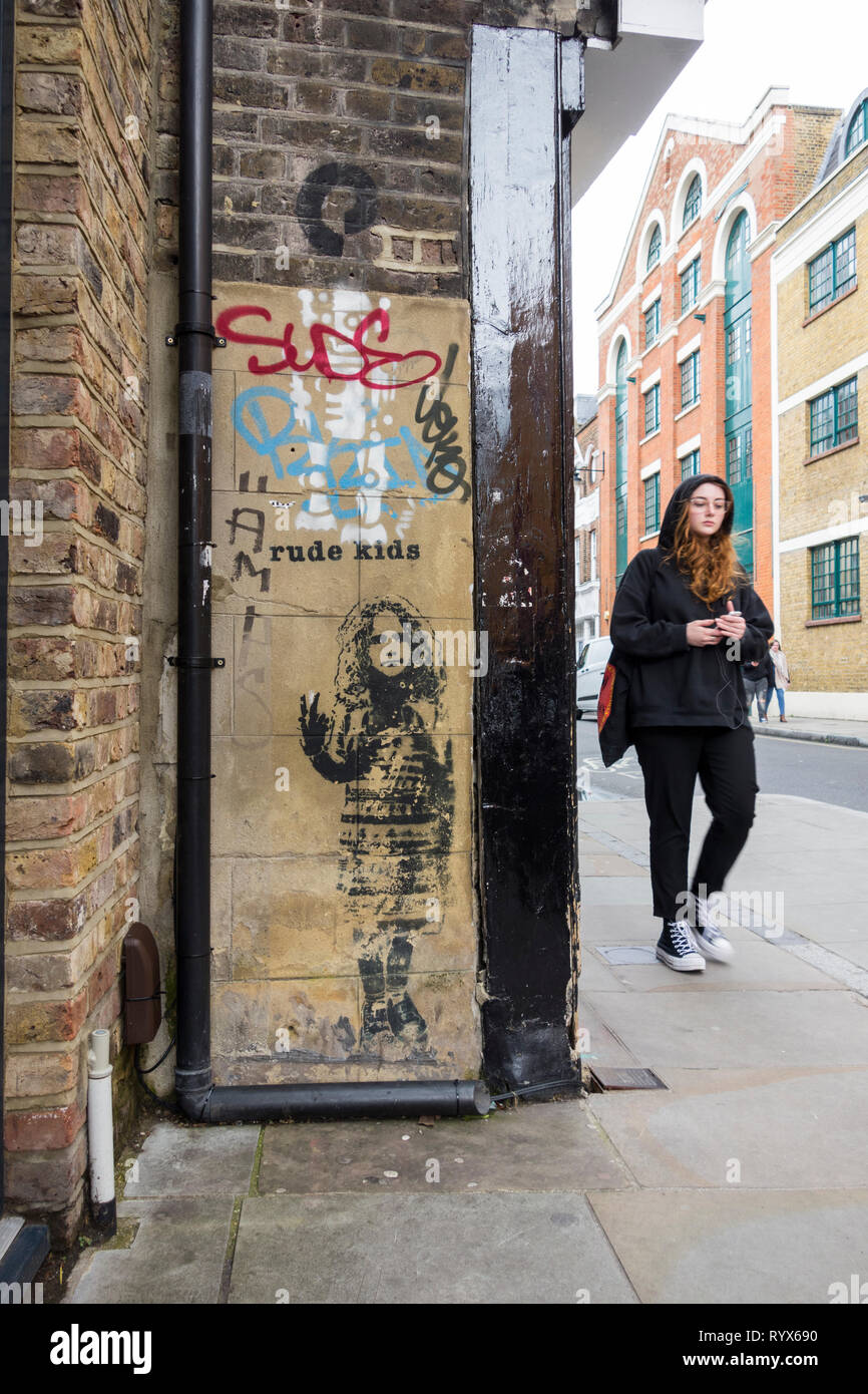 A young woman wearing a hoodie walking past a piece of Rude Kids ...