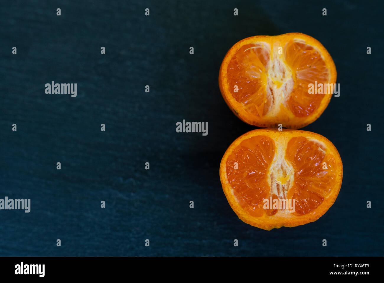 satsumas/orange/clementine close up on a dark slate background cut in half Stock Photo