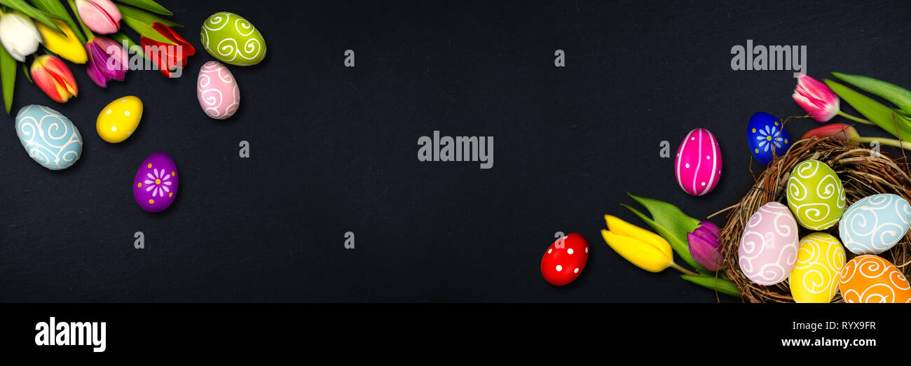 Colorful happy easter eggs in bird nest and tulips on dark empty slate ...