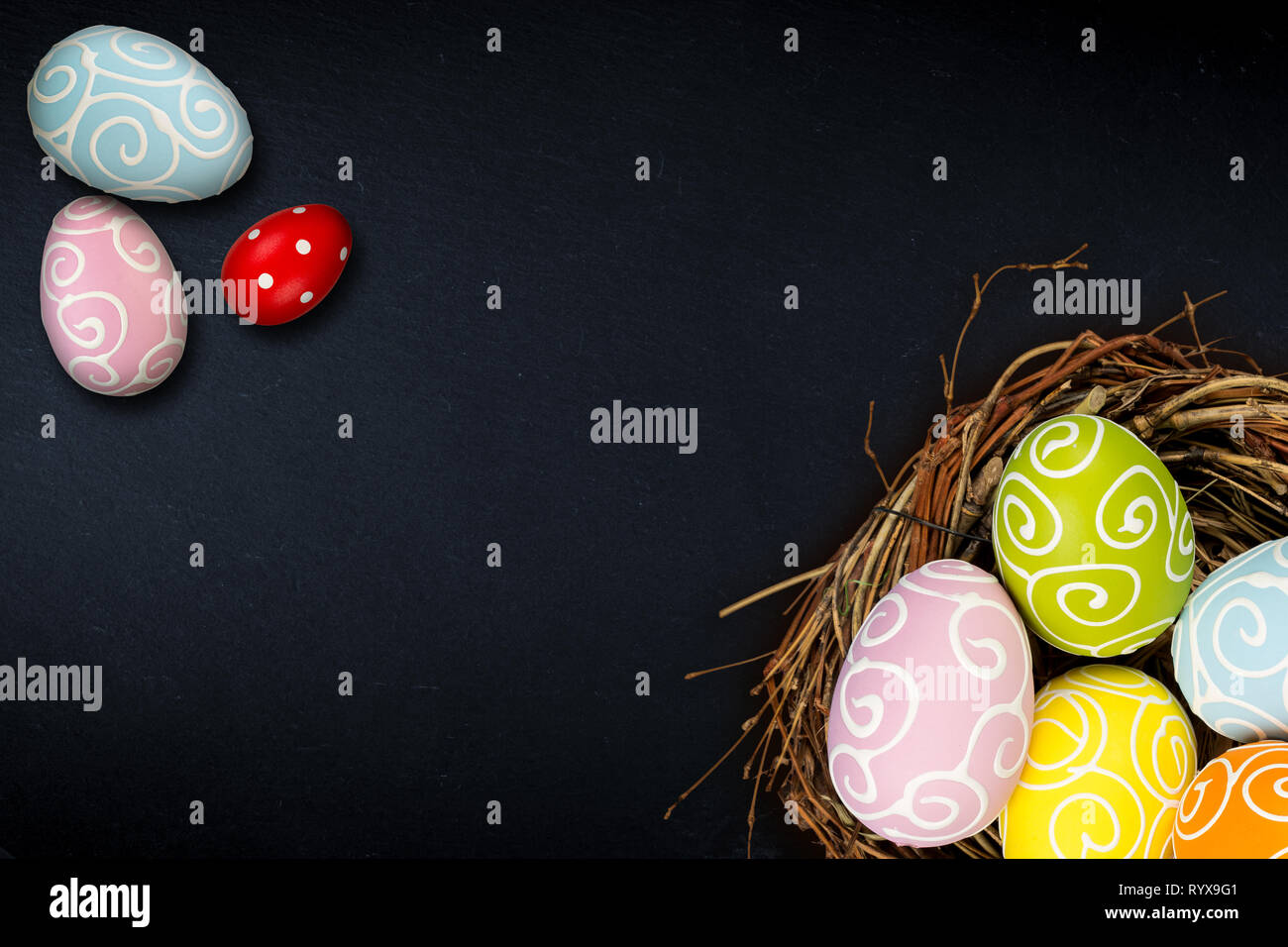 Colorful happy easter eggs in bird nest and tulips on dark empty slate ...