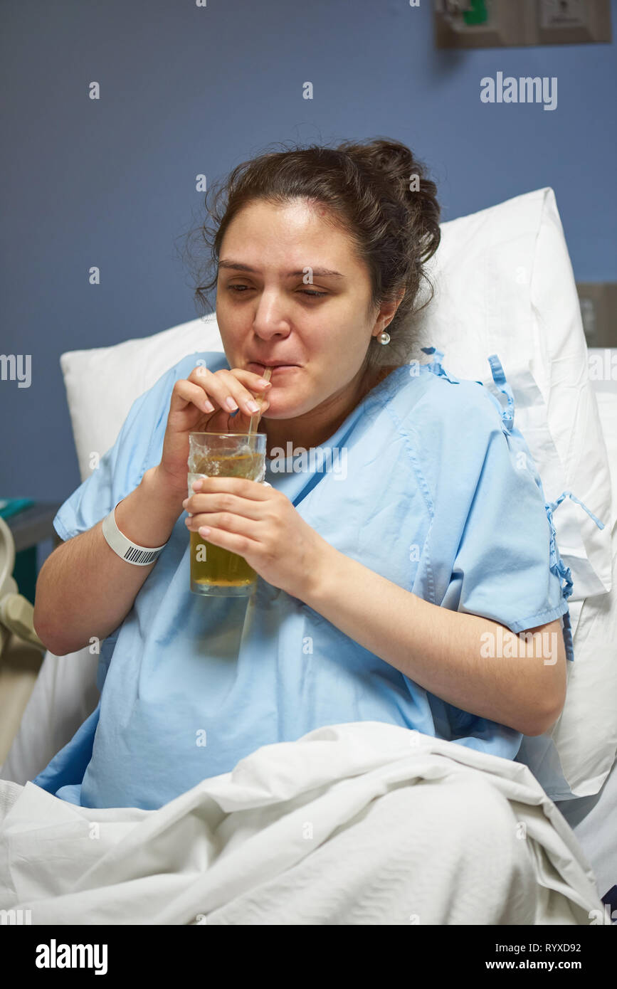 Woman drinking juice in clinic bed. Recovery of patient theme Stock Photo
