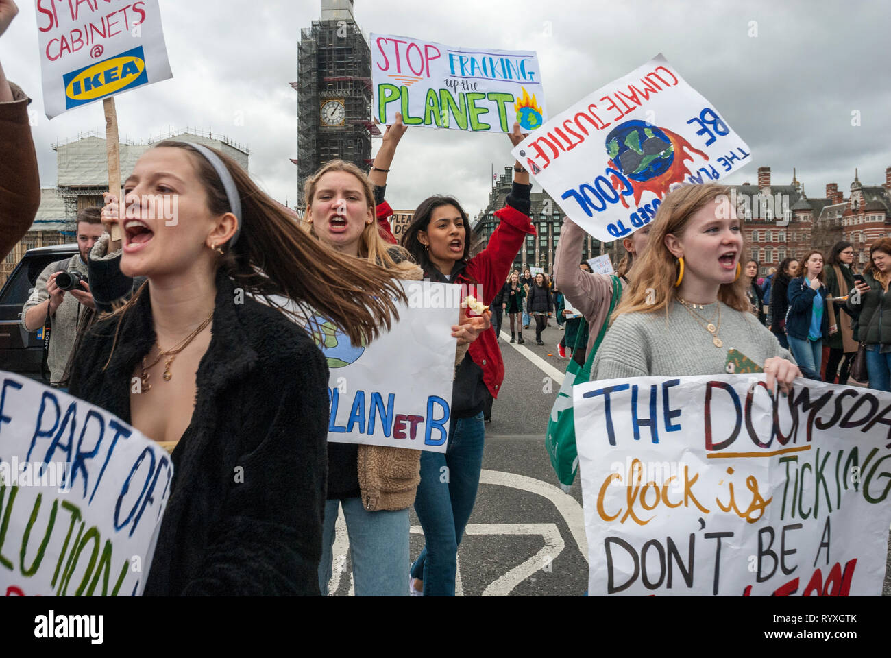 London, UK. 15th March, 2019. School students campaigning against climate change protest outside Parliament. Credit: Maggie sully/Alamy Live News. School children on strike to protest at climate change march over Westminster Bridge, London, with Big Ben in the background. In the foreground four lively young women sing and shout about global destruction with colourful banners 'Stop Fracking up the planet', 'Climate Justice', and 'The doomsday clock is ticking'.  Part of the worldwide 'FridaysforFuture' protest. Stock Photo