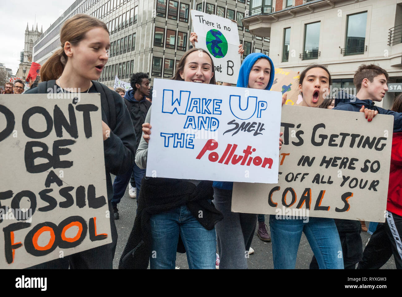London, UK. 15th March, 2019. School students campaigning against climate change protest outside Parliament. Credit: Maggie sully/Alamy Live News. School children on strike to protest at climate change rally outside Parliament, London. Four young women singing and shouting about climate justice and global warming with homemade posters 'Wake ups and smell the pollution', 'Don't a fossil FOOL', and 'Its getting hot in here so take off all your COALS'.  Part of the worldwide 'FridaysforFuture' protest. Stock Photo