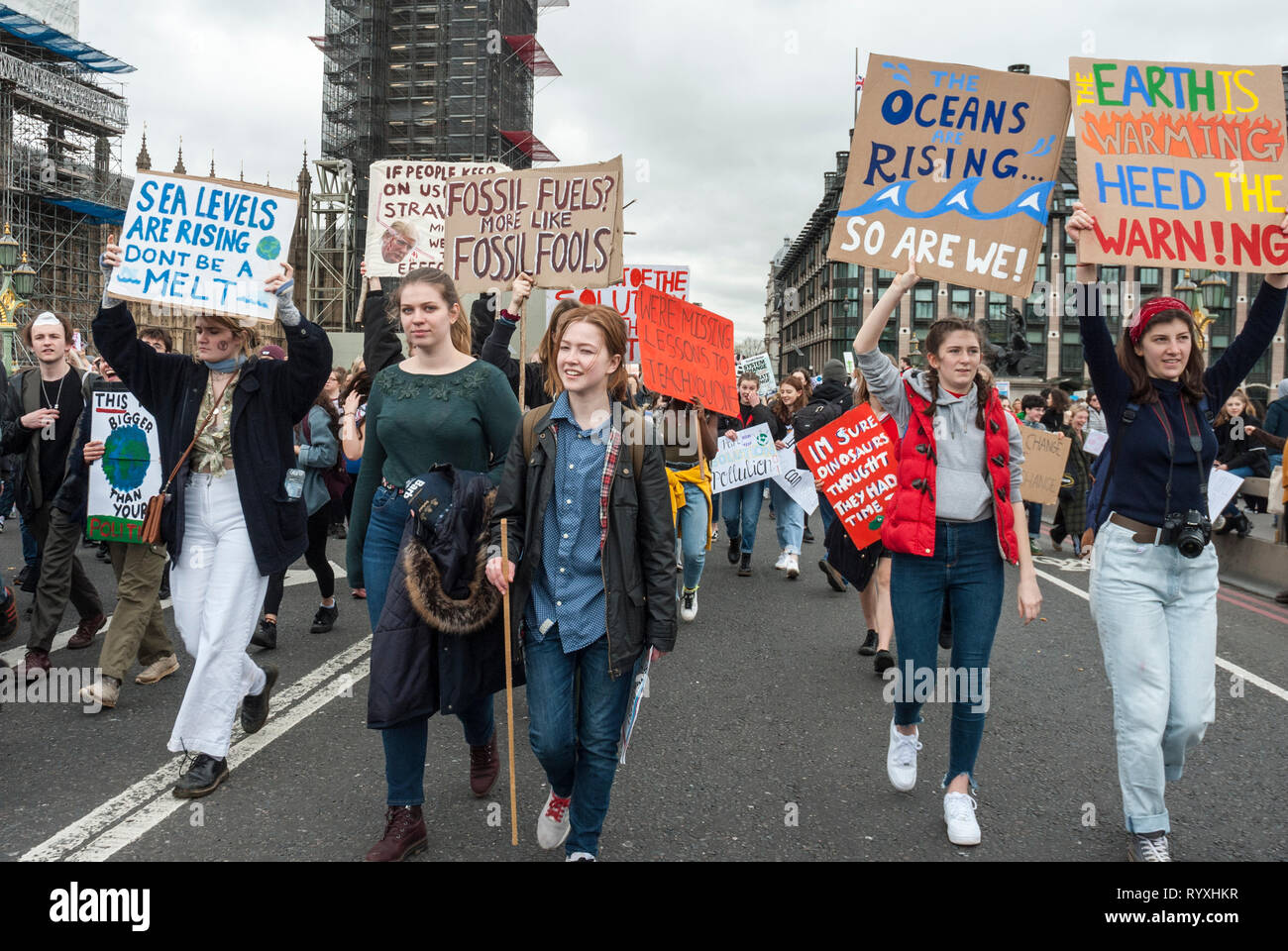 London, UK. 15th March, 2019. School students campaigning against climate change protest outside Parliament. Credit: Maggie sully/Alamy Live News. School children on strike, part of the 'FridaysforFuture'protest against climate change march over Westminster bridge, outside Parliament, London. In the foreground five young women students carry colourful homemade banners 'Oceans are rising, so are we', 'Fossil fuels? More like fossil fools', 'Sea levels are rising, don't be a melt' and 'The earth is warming, heed the warning'. Stock Photo