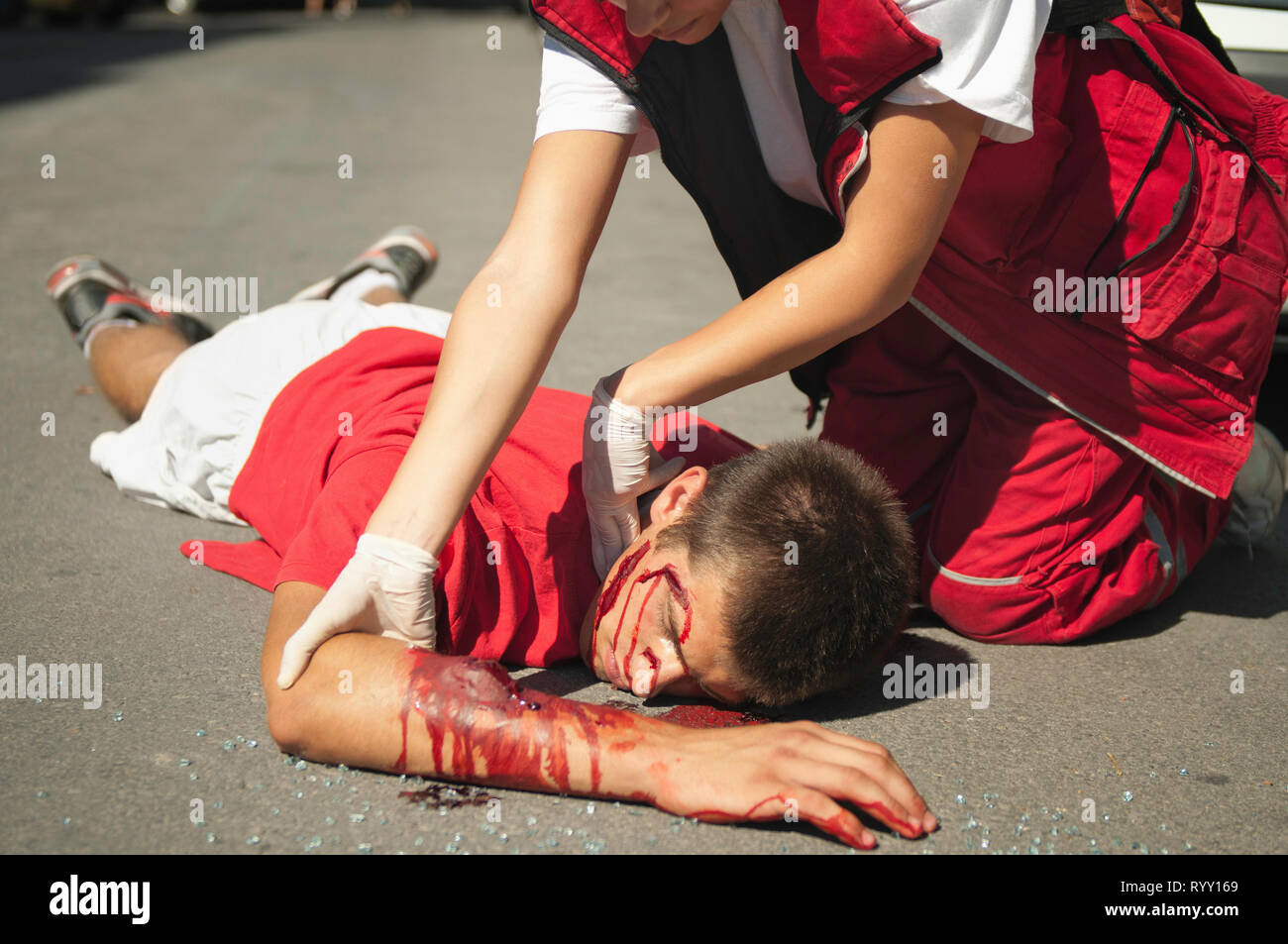 Paramedic with car accident victim on the street. Simulated exercise with doctor supervised realistic medical make-up. Stock Photo