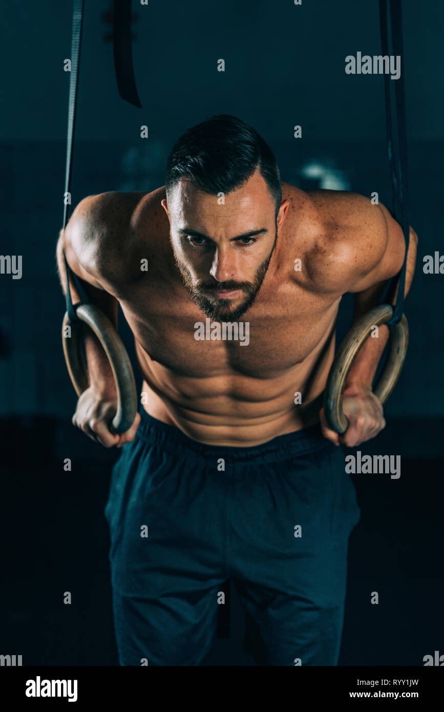 Athletic muscular male posing with gymnastic rings in a dark