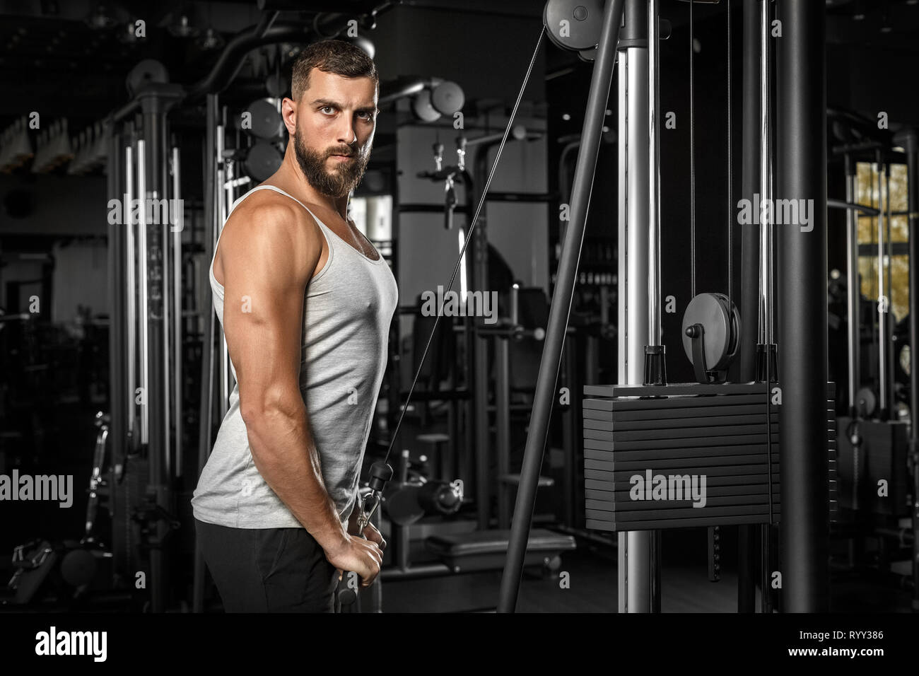 Bodybuilding. Bearded man standing doingcable straight arm pulldown at