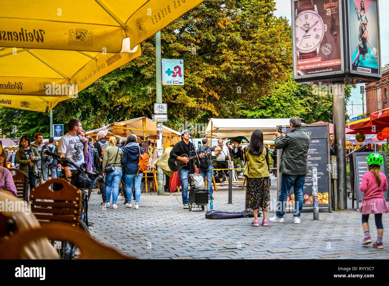 Tourists and local Germans enjoy a street performer singing and playing guitar in the outdoor Hackescher Markt square of Berlin Germany. Stock Photo