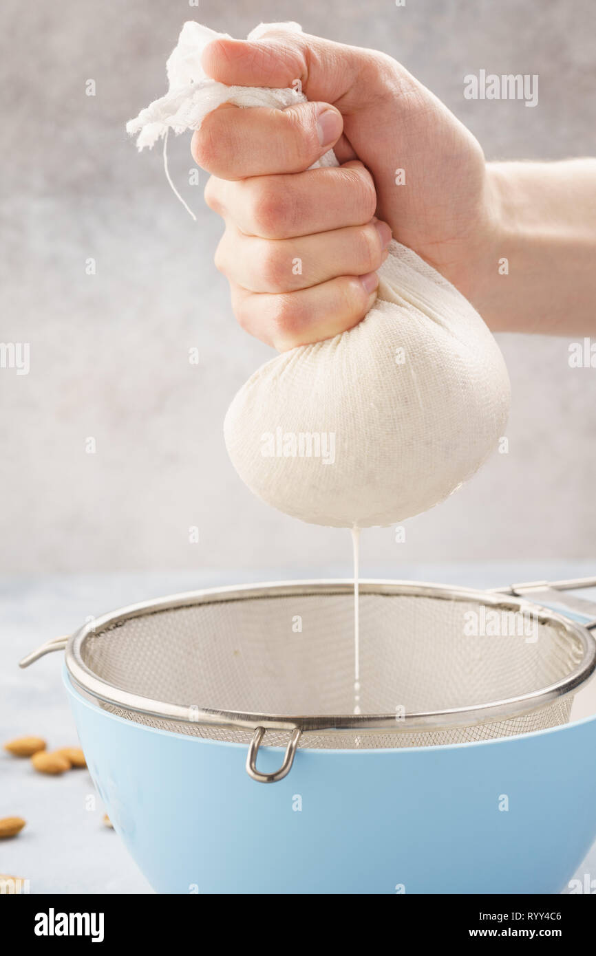 Homemade nut milk making process. Pouring milk into cloth and squeezing it to filter. Step by step recipe. Stock Photo