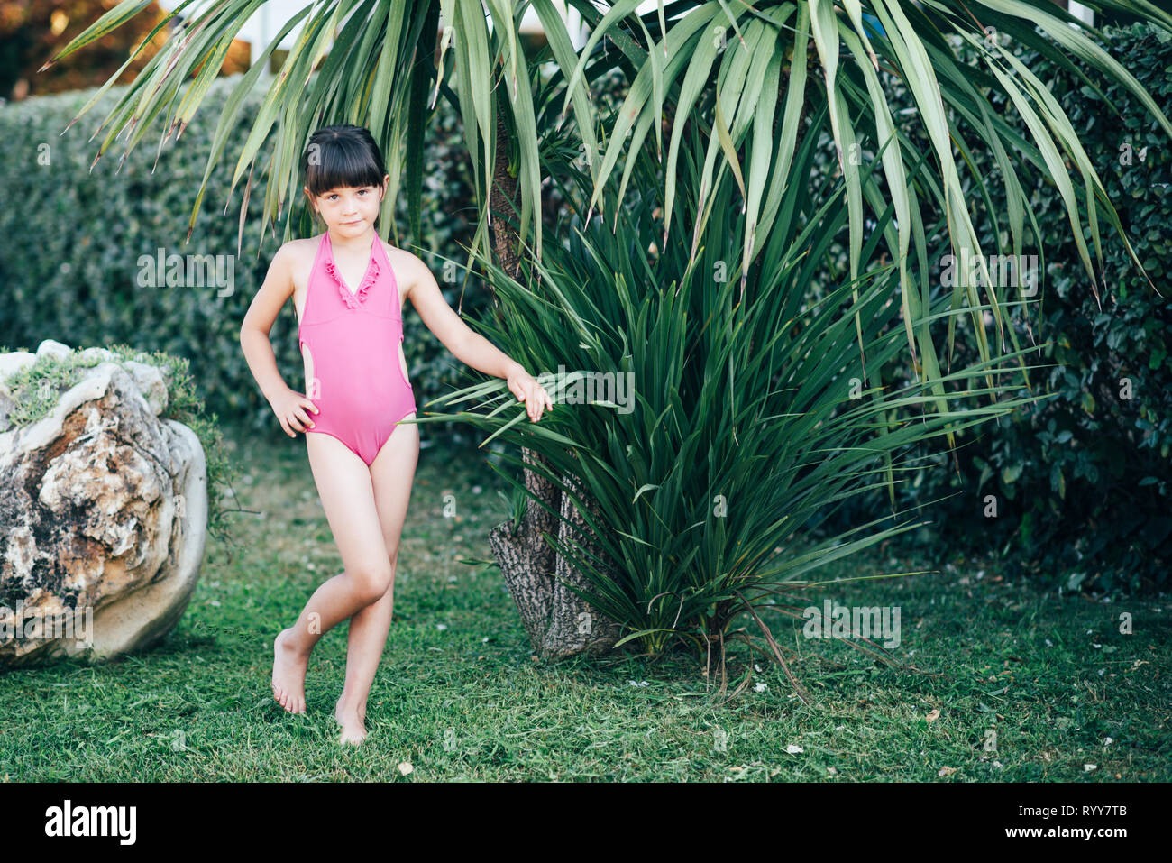 A cute little girl in a pink swimsuit is spending time in the nature in