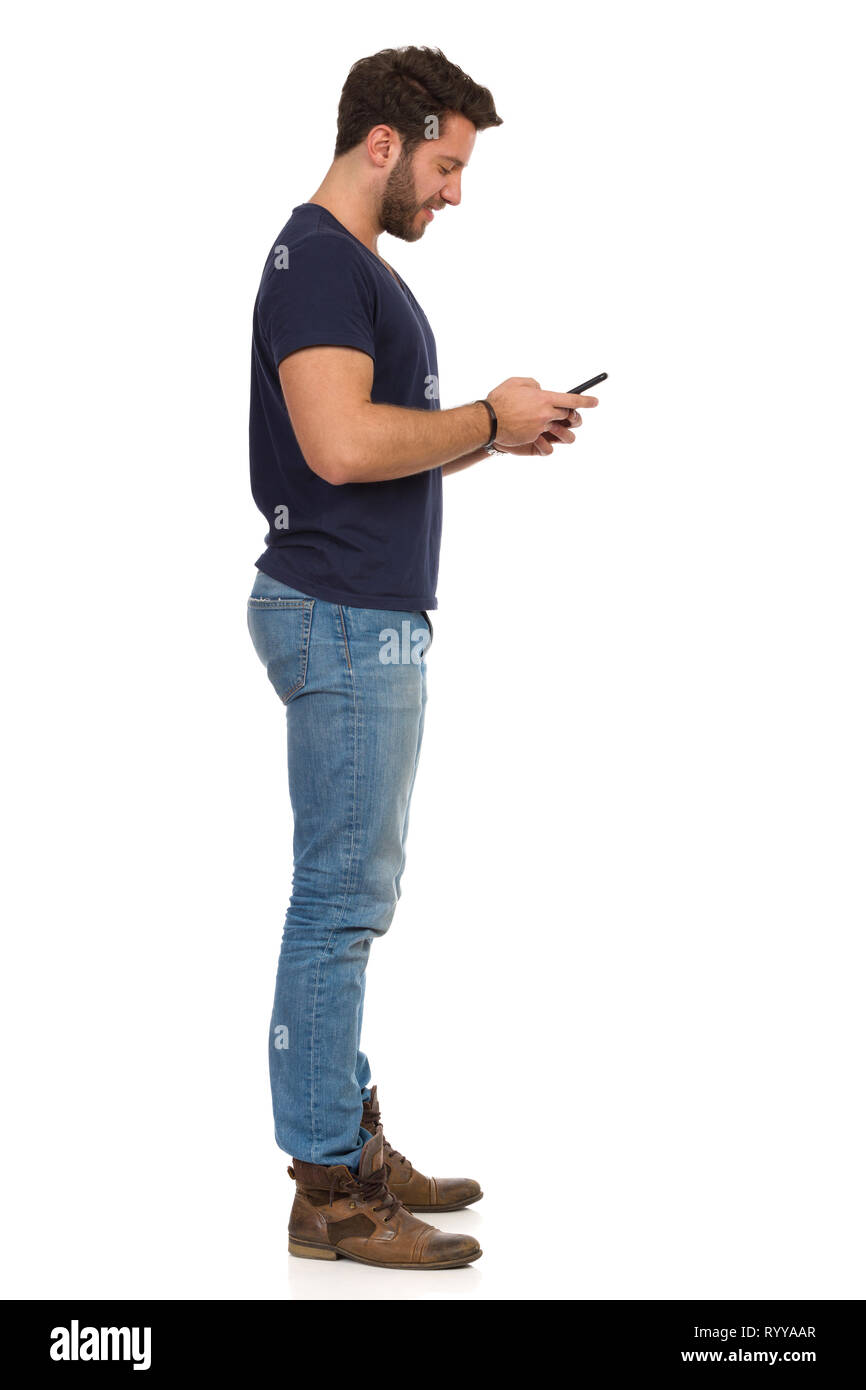 Man in jeans and blue t-shirt is standing and using telephone. Side view.  Full length studio shot isolated on white Stock Photo - Alamy