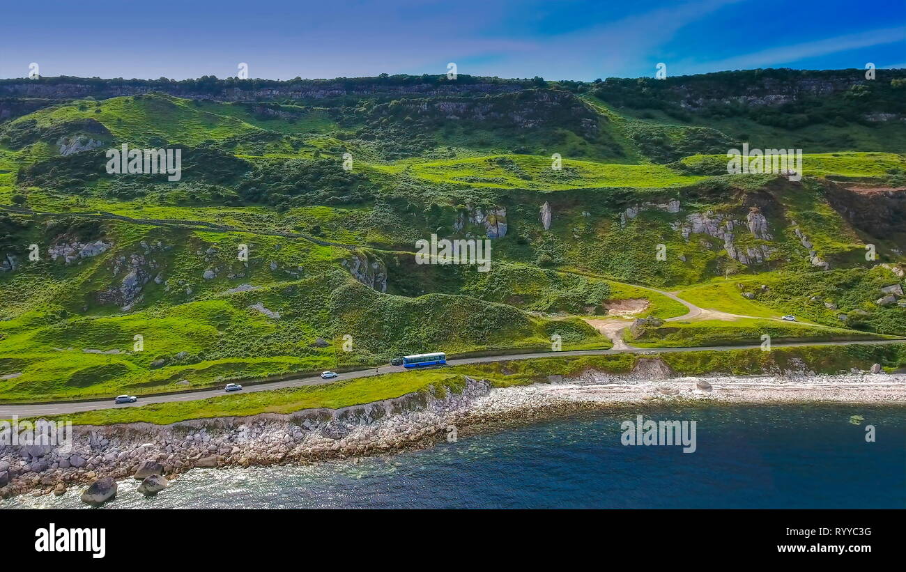 Aerial shot of the beautiful mountain in Cushendun Ireland there is a long road on the mountain side with a bus and cars travelling in Ireland Stock Photo