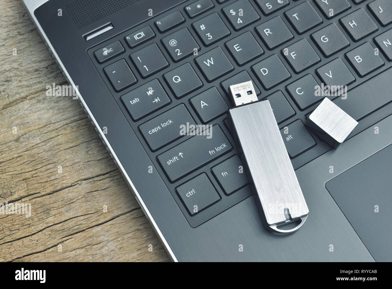 Close up of metal USB flash drive connected to laptop on wood desk Stock Photo