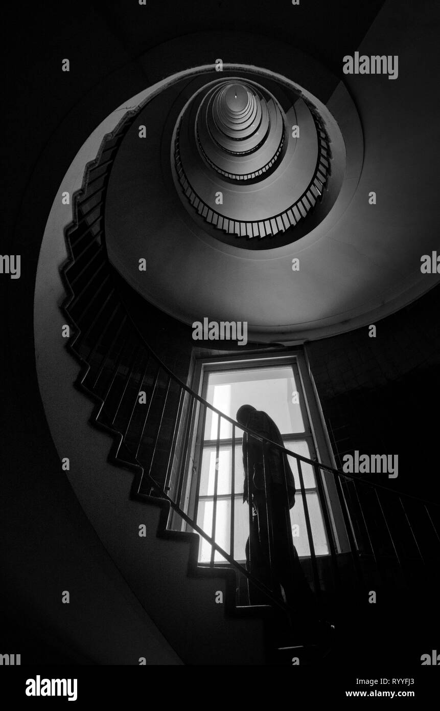 The silhouette of a man climbing the spiral staircase, dark black and white interior photography Stock Photo