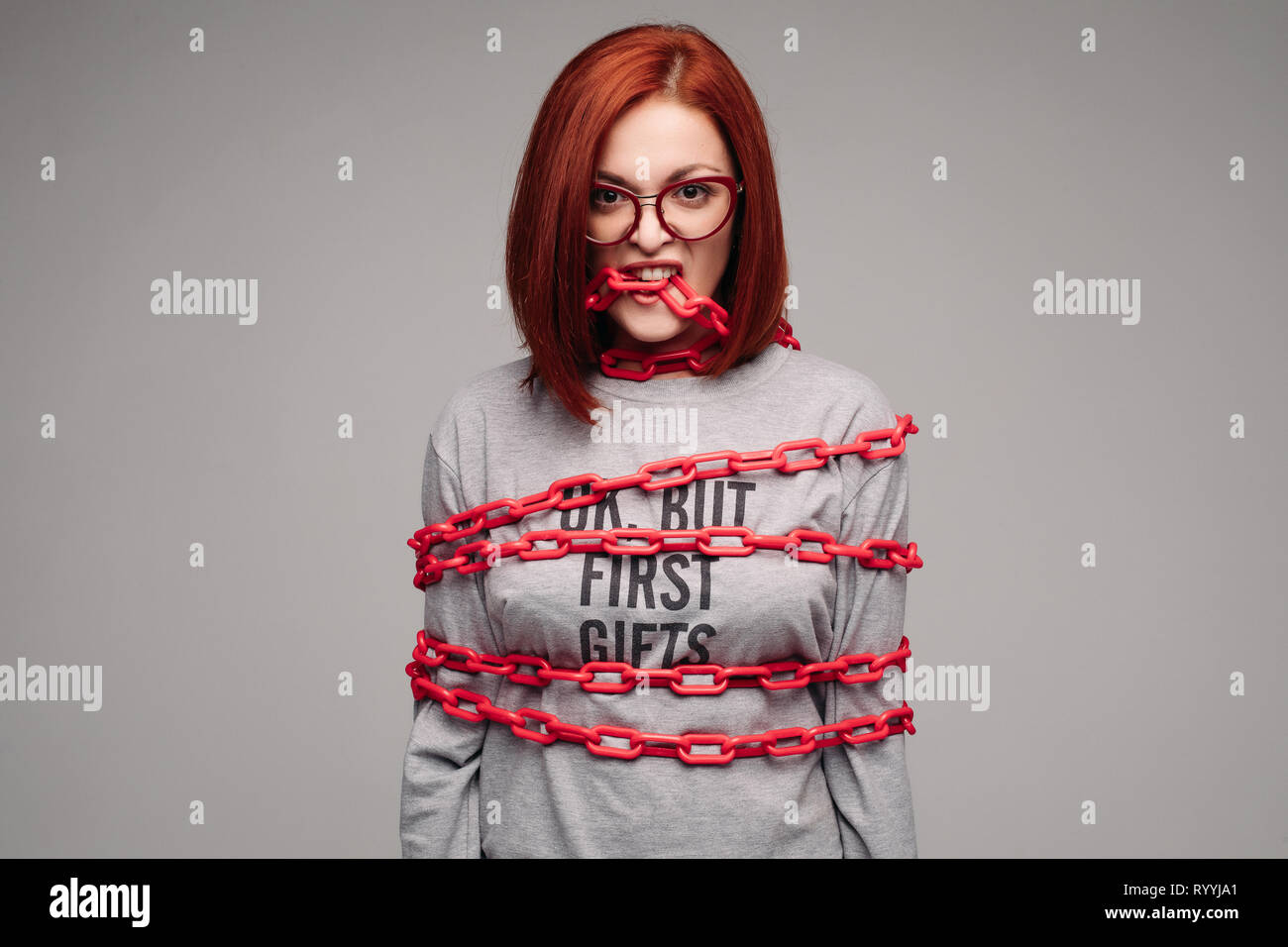 girl entangled in a chain,A red-haired woman with brown hair tries to get rid of the chain Stock Photo