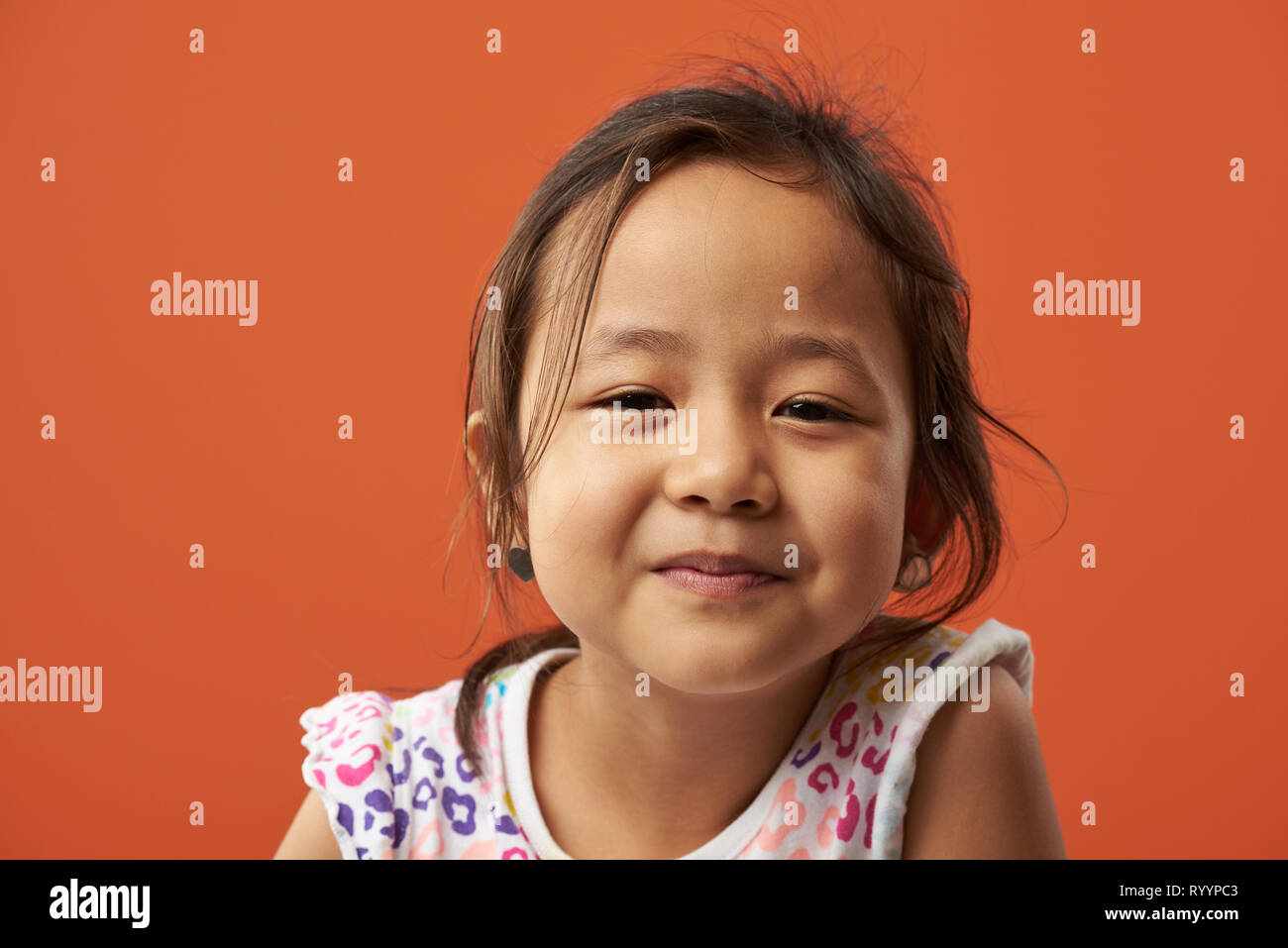 Portrait of serious asian little girl isolated on orange color background Stock Photo
