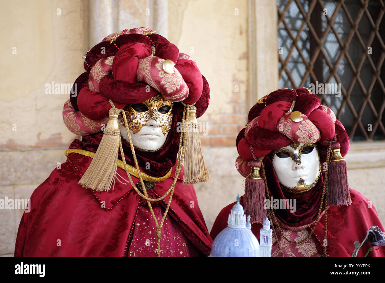 Man and woman dressed in traditional mask and costume for Venice Carnival standing under arch at Doge’s Palace, Piazza San Marco, Venice, Veneto, Ital Stock Photo