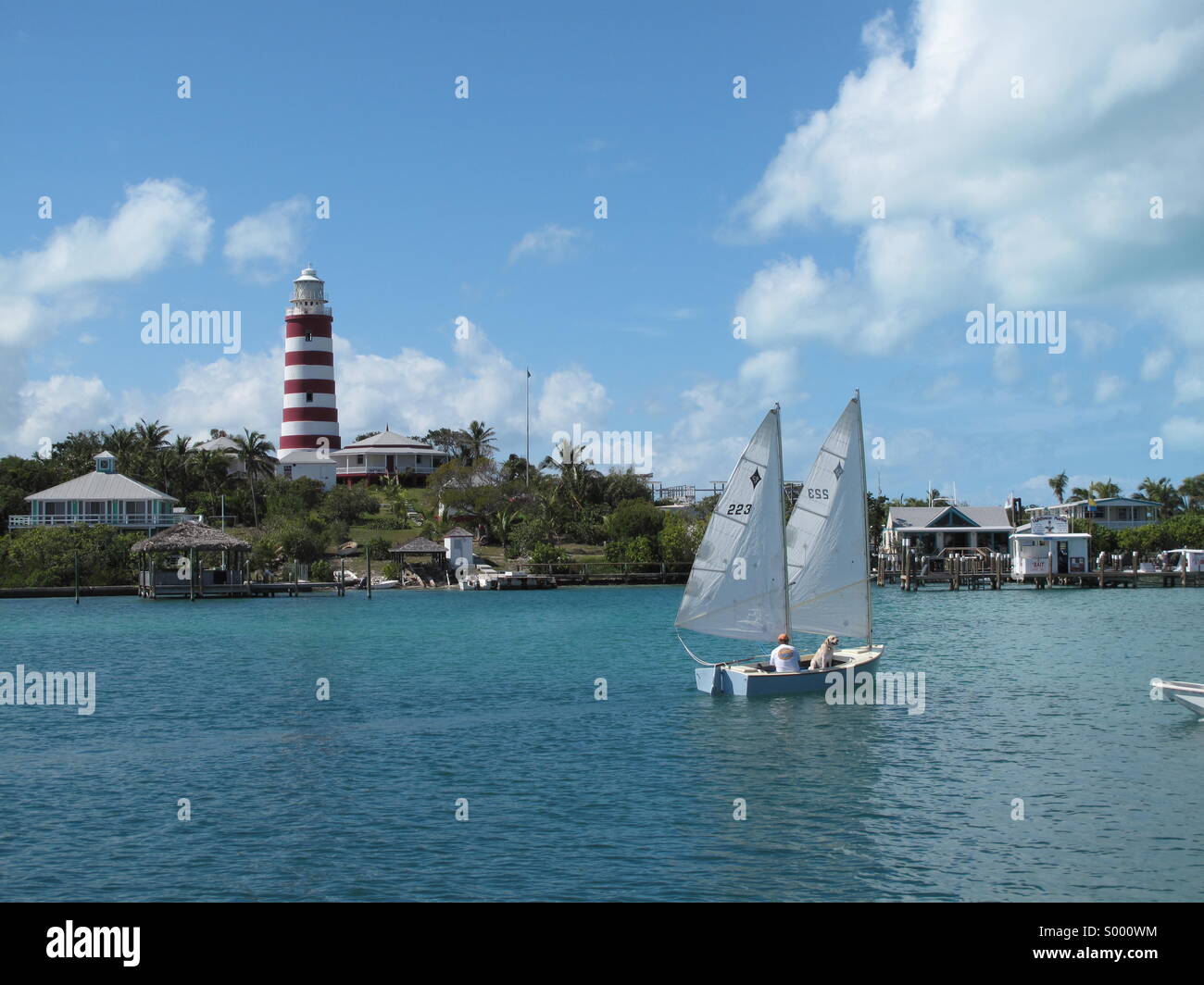 Two masted dinghy sails past the Hope Town Lighthouse. - Smartphone Captured Stock Image