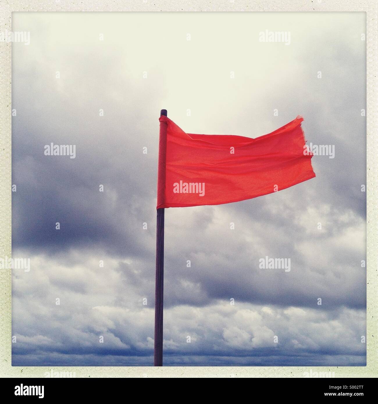 A red flag blowing at an ocean front beach. No swimming allowed Stock Photo