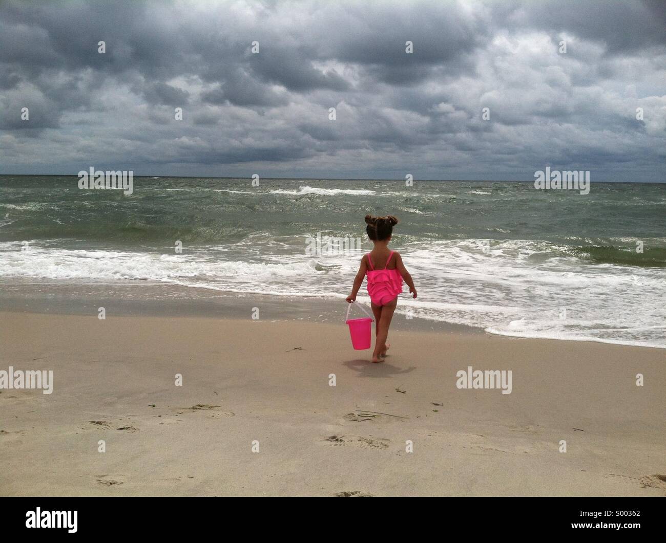A young girl in a pink bathing suit carrying a bucket at a ocean beach