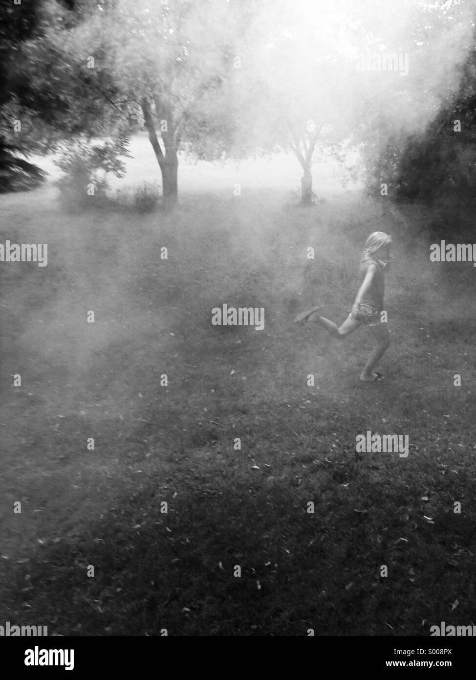The drifting smoke from fireworks casts a shroud over a girl running through a park. Stock Photo