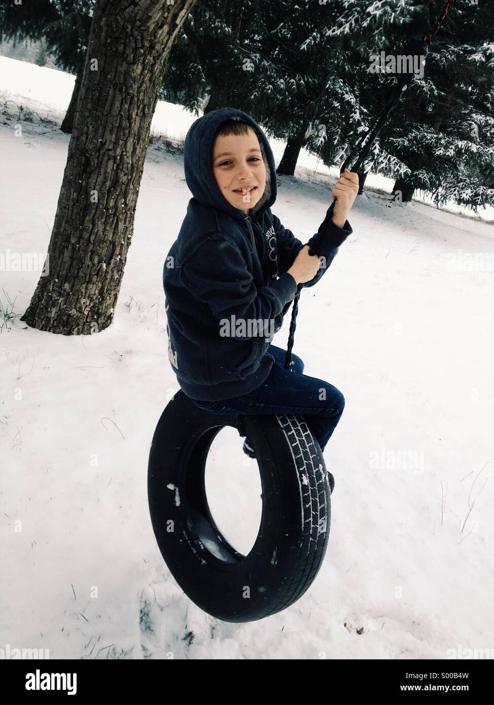 Boy on tire swing in winter Stock Photo