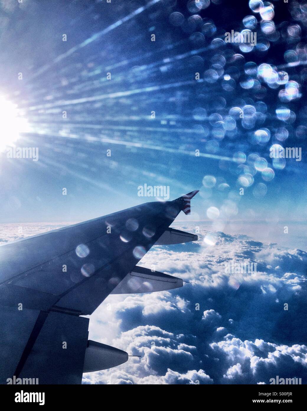 Looking through the airplane window, sun flare over the wing in a cloudy blue sky Stock Photo