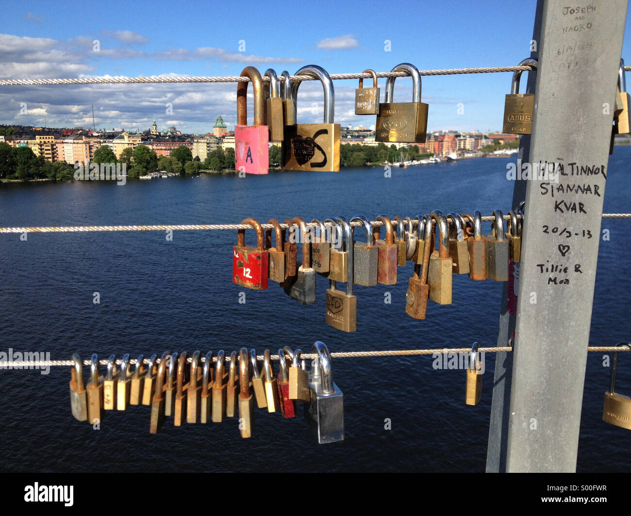 Love padlocks hanging on vasterbron west bridge in Stockholm with view to city over lake. - Smartphone Captured Stock Image