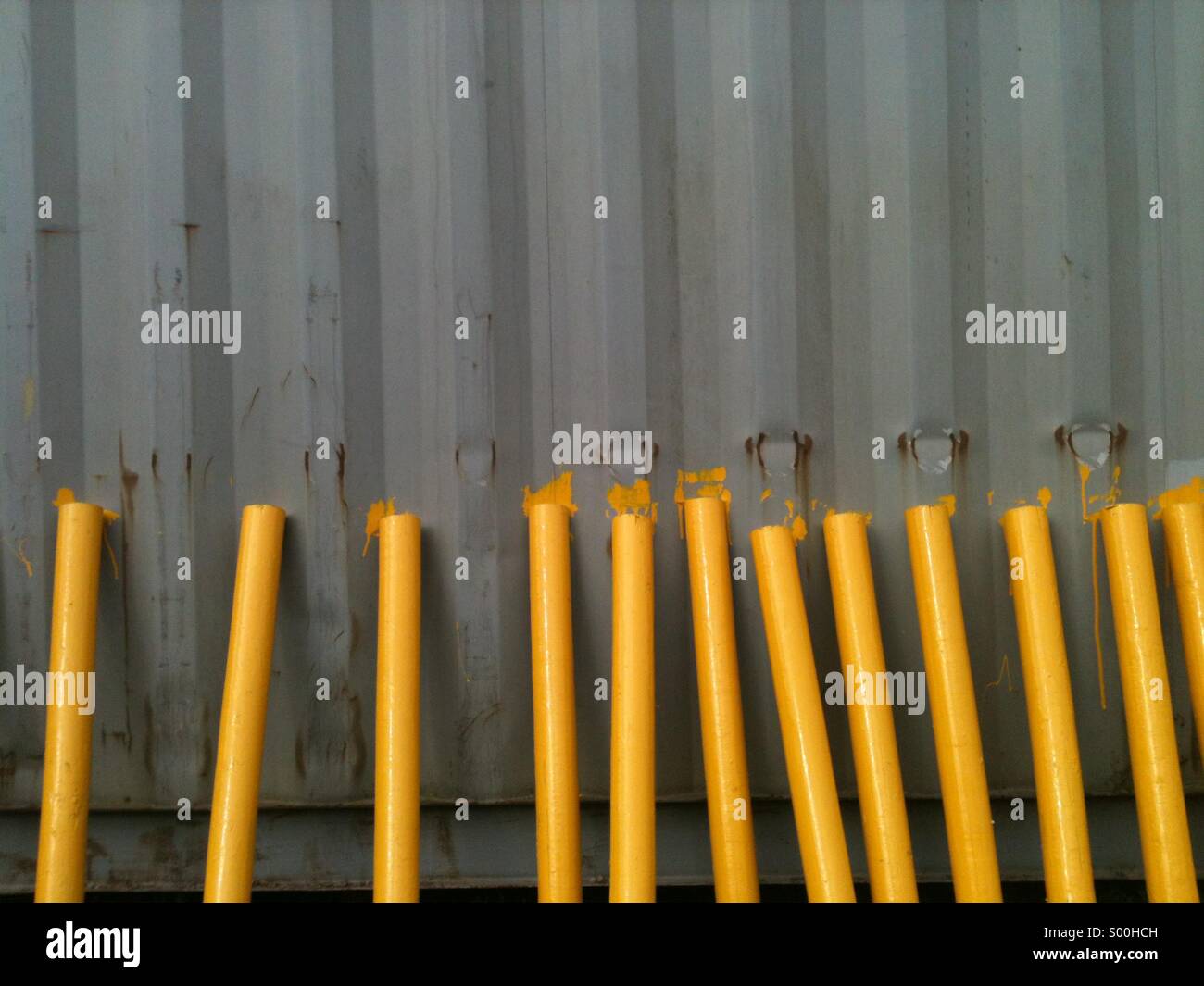 Wooden stakes freshly painted yellow against a grey metal background. Marker posts for golf course. - Smartphone Captured Stock Image