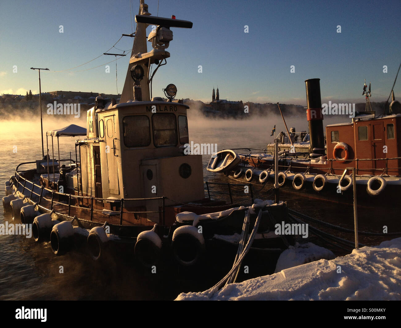 Old boat moored in central Stockholm at dawn with mist rising from winter water. - Smartphone Captured Stock Image