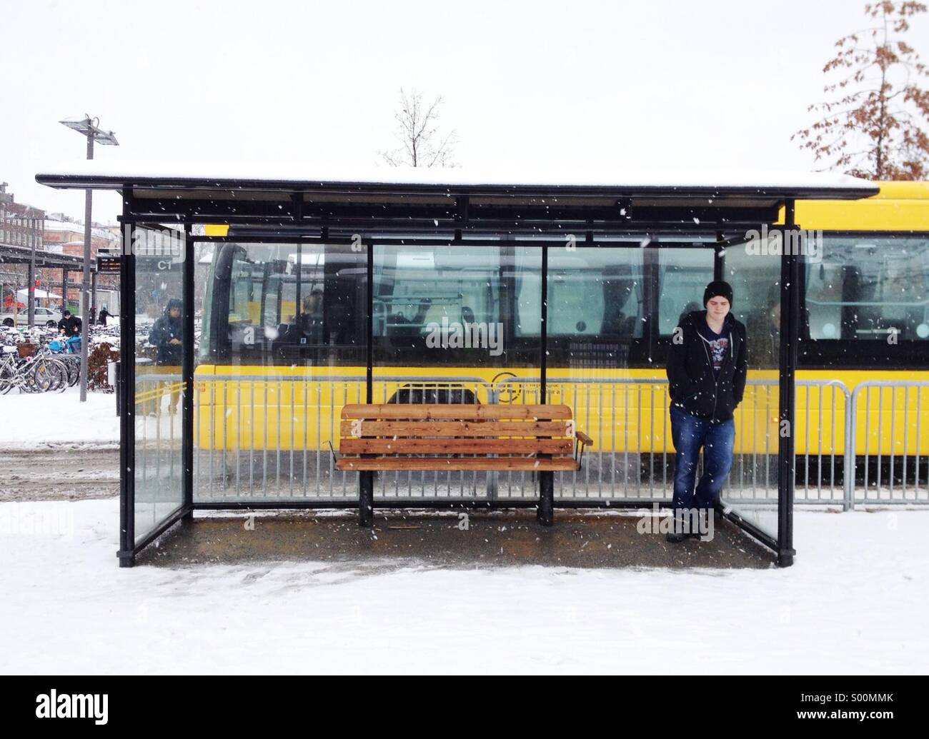 Young man stands waiting for bus in wet snow in Sweden. Stock Photo