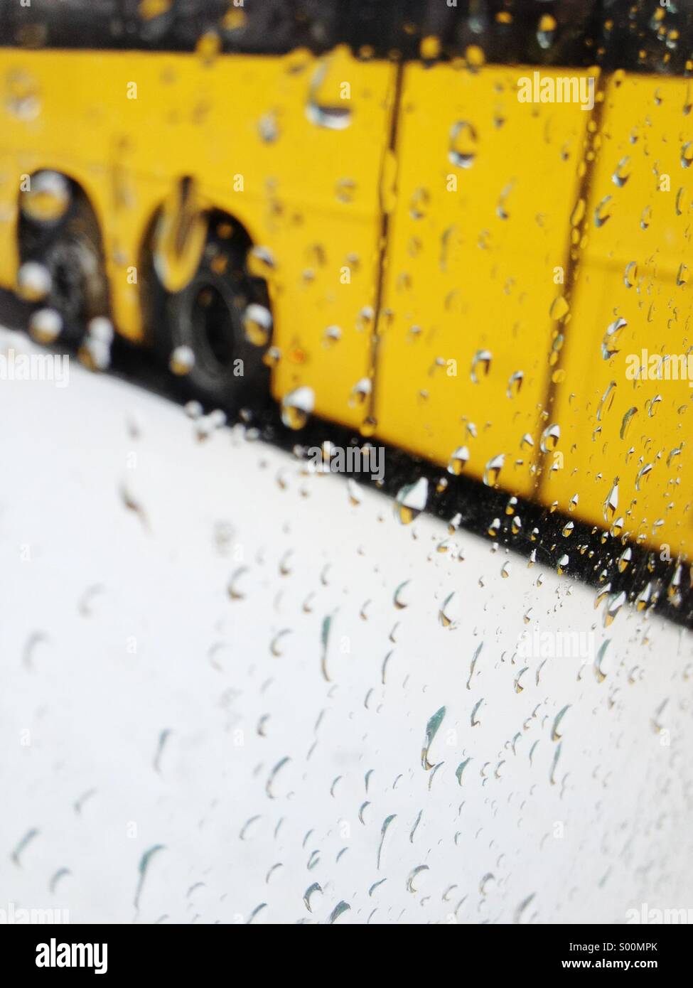 Yellow bus blurred behind water drops on window from wet snow and rain. Stock Photo