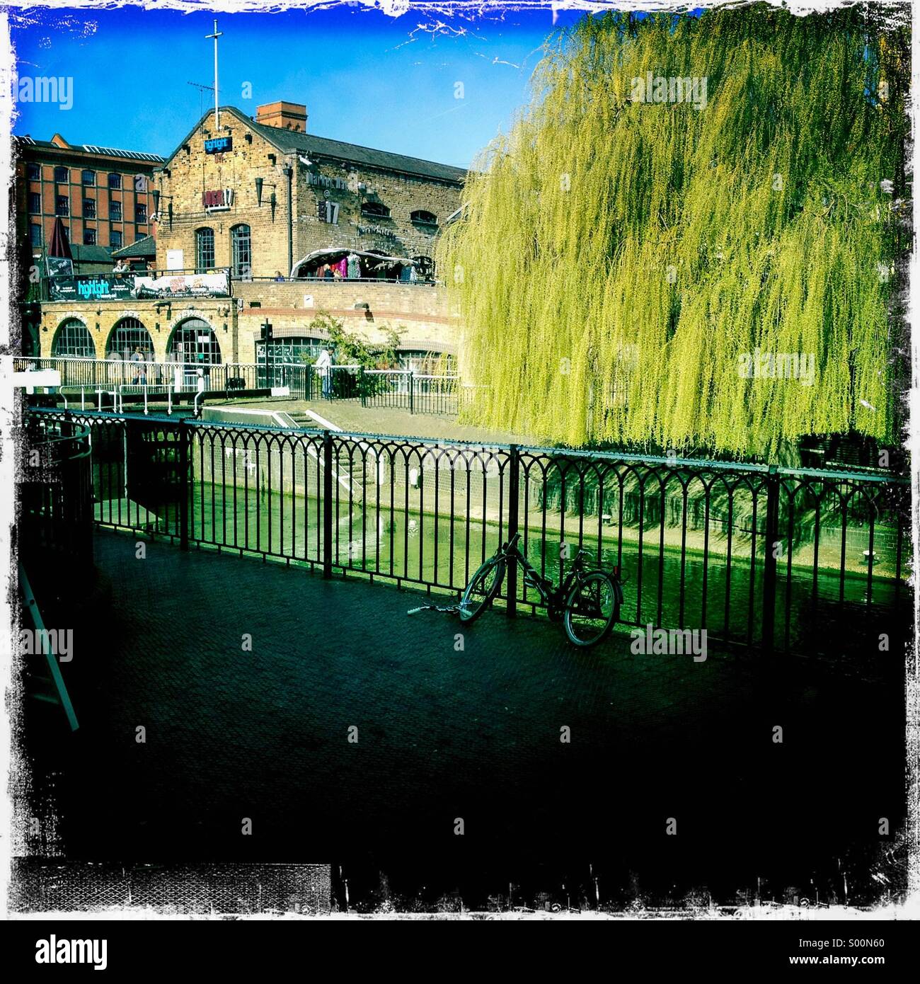 Camden Lock, Camden Town , London UK. Scene from bridge looking over lock with willow tree in mid ground and iron railings in the foreground. Hipstamatic, iPhone. Photo with white borders. Stock Photo