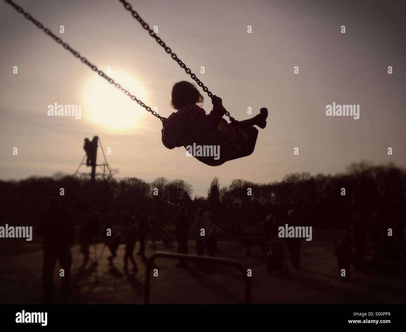 Girl swings high in playground against bright winter sun Stock Photo