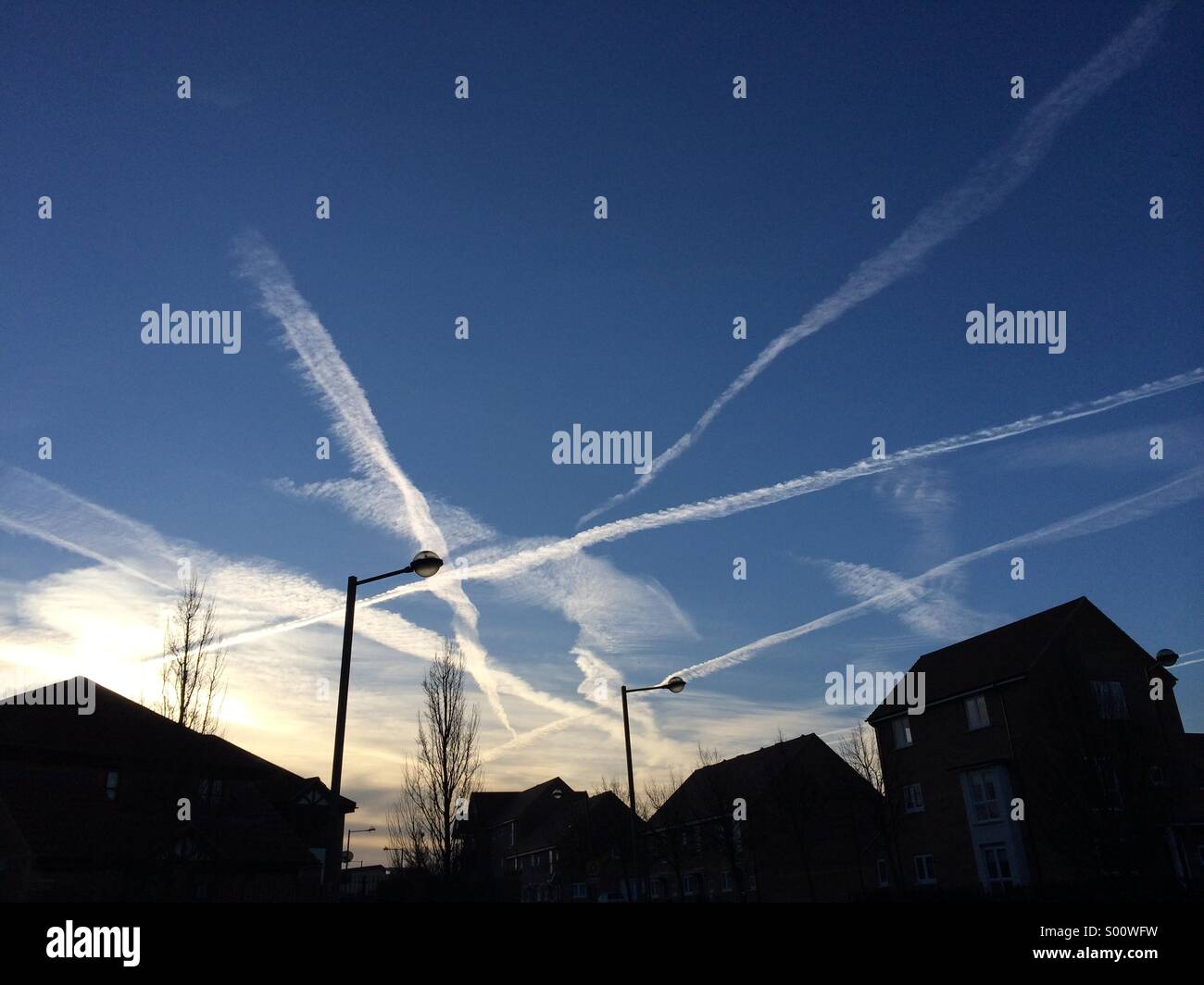 Vapour trails over housing estate at sunrise Stock Photo